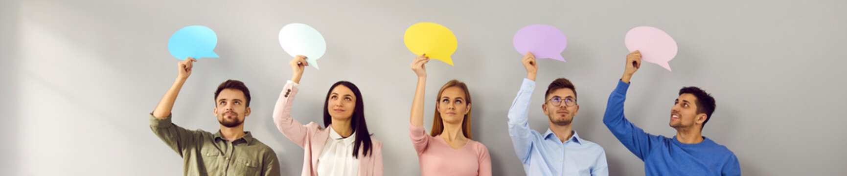 Group of happy young people standing in row and holding empty oval colorful mock up message bubbles. Team of male and female students or employees showing mockup speech balloons for sharing opinions