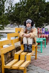 a cute six-year-old girl in a beige fur coat made of eco-friendly faux fur is sitting on a bench