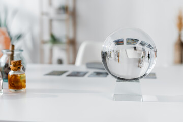 Glass orb near blurred witchcraft supplies on table.