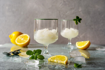 Lemon sorbet in two glasses with lemons, ice cubes, mint leaves on grey background - obrazy, fototapety, plakaty