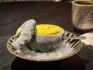A frozen small green pumpkin filled with orange ice cream on a plate with ice