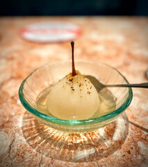 Whole pear dessert in sugar syrup with gold flakes sprinkled on top in a glass bowl with spoon