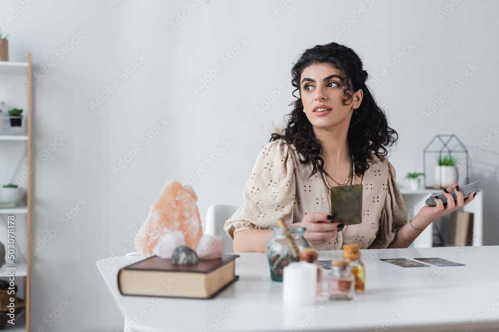 Wall mural smiling gypsy medium holding tarot cards near blurred book and crystals on table.