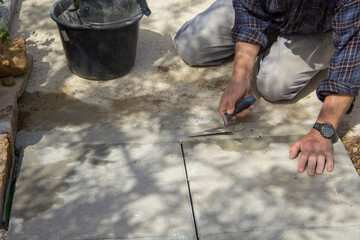 Image of the hands of an elderly bricklayer who, with a trowel and concrete, builds a path in the...