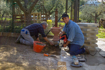 
Image of a young man and an elderly bricklayer building a driveway in their backyard using a...