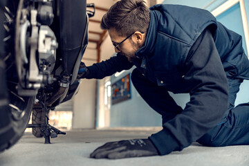 A service worker in garage checking on motor bike.