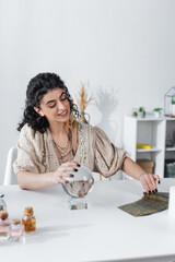 Smiling gypsy medium touching magic orb and tarot cards on table.