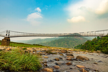 isolated iron suspension bridge over flowing river with mountain and blue sky background at morning