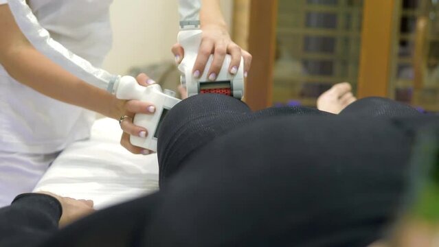 Close-up of LPG massage in a beauty salon. A male client in a special black suit gets an anti-cellulite. A doctor manipulating a hardware cosmetology gadget.Body care.Hardware correction of the figure