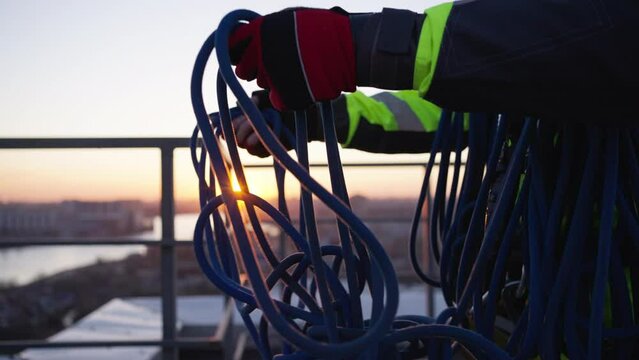 Skein of rope in hands of professional climber in special equipment. Industrial climber tries to untangle blue safety rope at sunset closeup