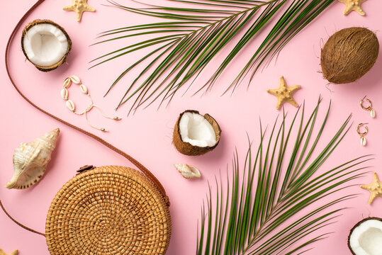 Summer holidays concept. Top view photo of round rattan handbag coconuts shell bracelet earrings starfishes and palm leaves on isolated pastel pink background