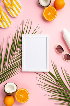 Summer concept. Top view vertical photo of white frame sunglasses sunscreen bottle yellow flip-flops coconuts oranges and palm leaves on isolated pastel pink background with blank space