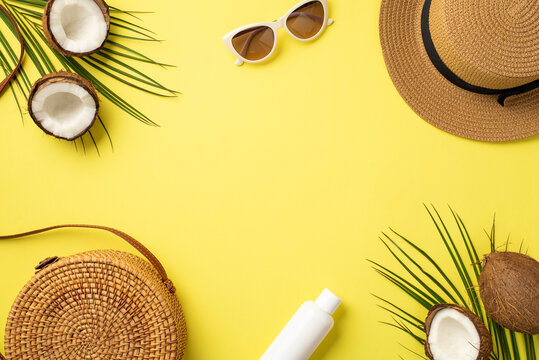 Summer concept. Top view photo of hat round rattan bag sunglasses sunscreen bottle cracked coconuts and palm leaves on isolated yellow background with copyspace in the middle