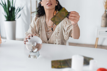 Cropped view of fortune teller holding tarot card and orb at home.