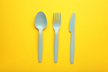 Blue plasic forks, spoons and knives on yellow background with copy space, top view.