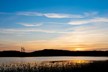 Sunset with reflections in water and silhouette of treeline. Bridge pylons in distance.