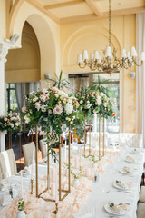 banquet tables with white tablecloths are in the hall of the old house, on the tables are flower arrangements, candles, plates with napkins, glasses and cutlery