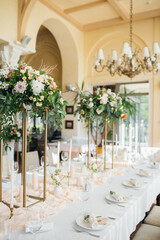 banquet tables with white tablecloths are in the hall of the old house, on the tables are flower arrangements, candles, plates with napkins, glasses and cutlery