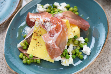 Close-up of open lasagna with prosciutto, ricotta and crushed green peas on a turquoise plate, horizontal shot