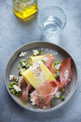 Plate with pea, ricotta and prosciutto open lasagna, vertical shot on a grey concrete background, elevated view