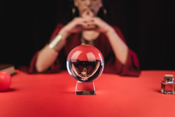 Cropped view of magic orb near blurred fortune teller isolated on black.