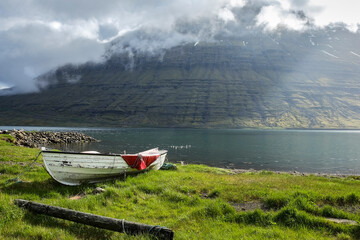 Rowboat moored on the grassy shore in Eskifjörður fjord, Iceland. cloud-covered Hólmatindur...
