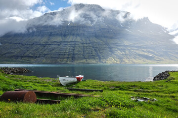 Rowboat moored on the grassy shore in Eskifjörður fjord, Iceland. cloud-covered Hólmatindur mountain in the background
