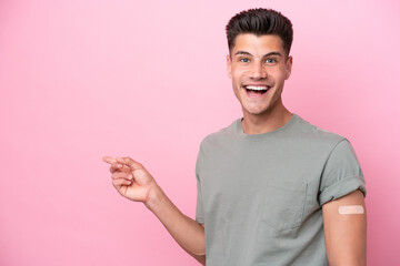 Young caucasian man wearing band-aids isolated on pink background surprised and pointing finger to the side