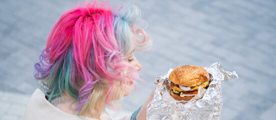 Naklejka premium Caucasian woman with curly colored hair eating burger. Bad eating habits and love of fast food