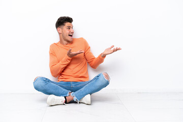 Young man sitting on the floor isolated on white background with surprise facial expression