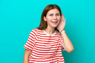 Fototapeta premium Young English woman isolated on blue background listening to something by putting hand on the ear