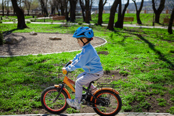 Naklejka premium Adorable kid boy in blue helmet and vest riding on bicycle in the forest