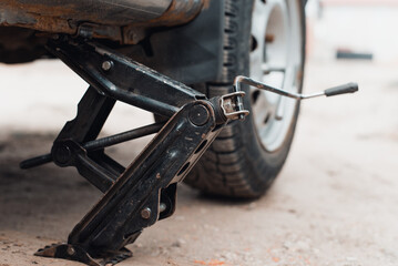 Broken car repair or seasonal wheel change concept. Close-up of car standing on jack, outdoors. Selective focus on equipment