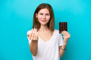 Young English woman with chocolat isolated on blue background inviting to come with hand. Happy that you came