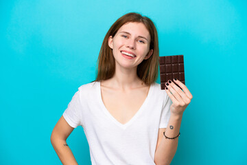 Young English woman isolated on blue background taking a chocolate tablet and happy