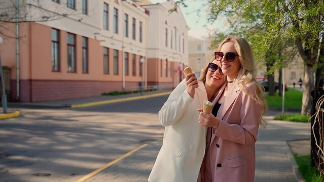 Two females hugging laugh and touch each other outdoors. Young adult women in sunglasses spending time outside. Girls with ice cream having fun in city park. Lesbian lgbt pair concept