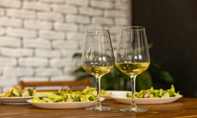 Two glasses with white wine and green salad with cucumber and radish daikon. An appetizer for a banquet or buffet. Grey tiled wall.