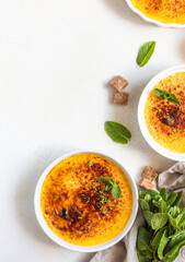 Creme brulee with caramel crust and mint in white ceramic dishes. Famous french dessert. Delicious desserts for cafe or restaurant.