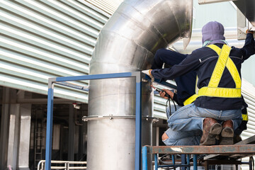 Welder wearing personal protective equipment (PPE) gas pipe repair welding in industrial plant.