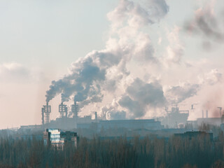 Smoke from chimneys at the plant in the rays of the sunset as a background.