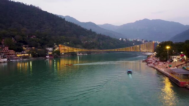 iron suspension bridge illuminated with ferry lights with ganges riverbank view at evening