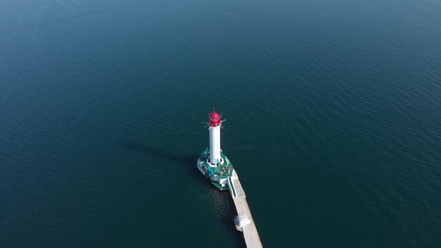 Beautiful old lighthouse in Odessa Ukraine. Black Sea turquoise water drone orbit high angle shot. People stand at lighthouse