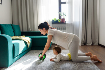Young mom do exercises with her baby at living room.