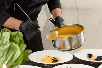 chef prepares carrot cream soup with seafood in a restaurant