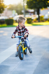 stylish European boy in shirt and jeans rides balance bike on asphalt. Child riding without helmet