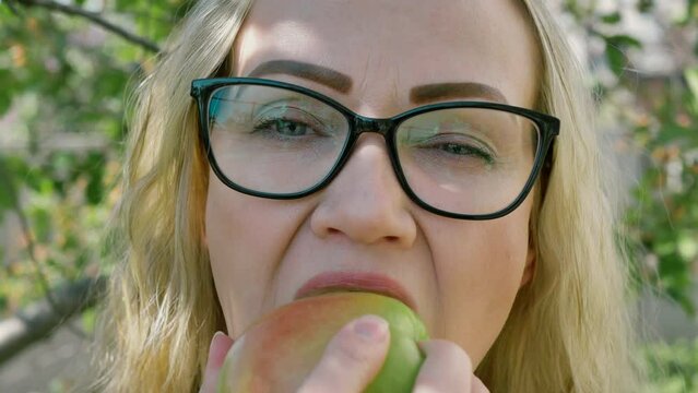 portrait of a young woman biting and eating a ripe green apple, looking at the camera in the garden, slow motion. Healthy food and beauty. diet