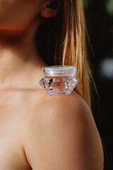 Aesthetic photo of transparent small jars of cosmetics on the shoulders of a girl