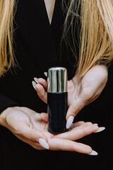 Fototapeta premium Black jar with silver lid spray cosmetics in the hands of a girl on a body background