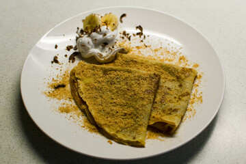 Two sprinkled crepes and pieces of banana on whipped cream on white plate