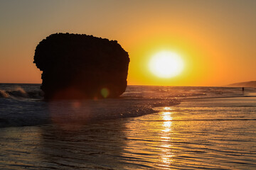 amazing sunset over the ocean and waves crashing against a large rock called Tower of Gold on the...